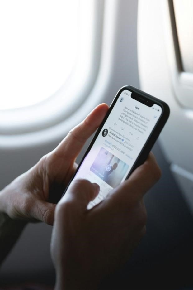 A Broadcast Journalist Scrolls Through Their Newsfeed on a Plane